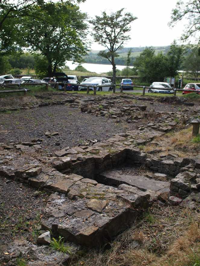 Picture shows the foundations of the original church; in the background is a car park and the Stocks Reservoir